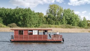 Une péniche à usage résidentiel, dotée d’une structure extérieure en bois, d’une terrasse couverte et d’une enseigne.