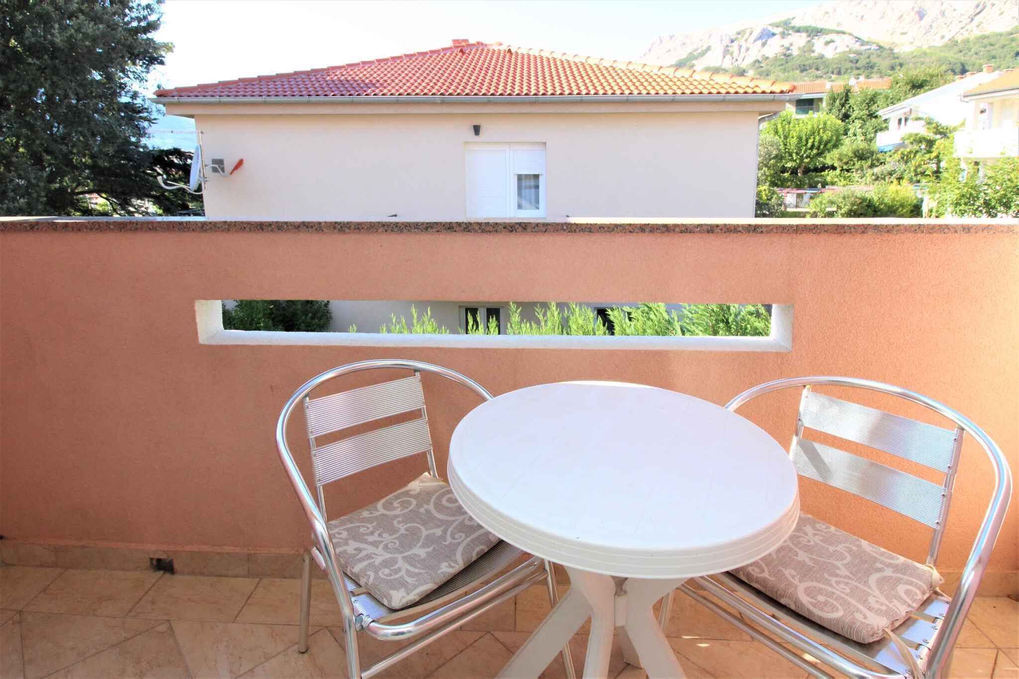 Un balcon avec deux chaises en métal et une petite table ronde, donnant sur un immeuble avec un toit rouge.