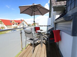 A balcony with a table and chairs, a large umbrella, and a view of houses in the background.