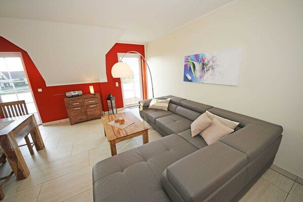 A modern living room with a grey sofa, wooden dining table, and a red accent wall.