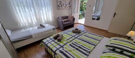 A bedroom with a bed, a sofa, a window with curtains, a painting, and a door.