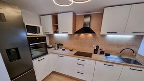 Une cuisine moderne avec des meubles blancs, un réfrigérateur en acier inoxydable, un four à micro-ondes, un four traditionnel, une cuisinière à gaz et un évier.
