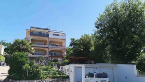 Un immeuble à plusieurs étages doté de balcons, d’un mur en pierre et d’une voiture blanche garée devant.