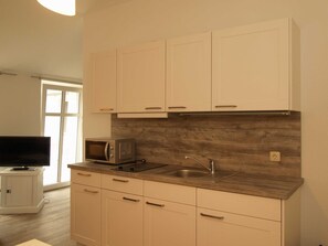 A kitchen with white cabinets, a microwave, a sink, and a television on a stand.