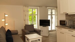 Ett vardagsrum med en soffa, ett litet bord, en tv och en köksdel med skåp och en mikrovågsugn.