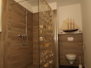 A bathroom with a glass shower enclosure, a toilet, and a ship model on the wall.