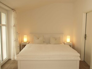 A bedroom with a bed, two bedside lamps, a window with curtains, and a door.