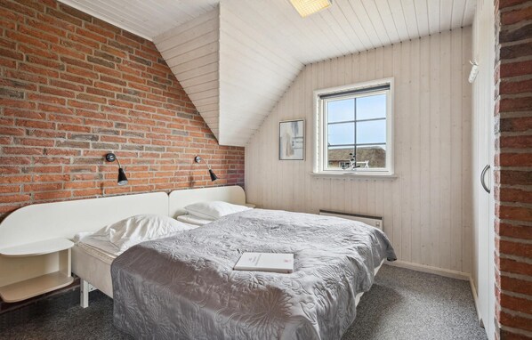 A bedroom with a brick wall, a sloped ceiling, a window, a bed, a bedside table, and a radiator. - Amazing home in Ringkøbing with sauna (Ringkøbing)