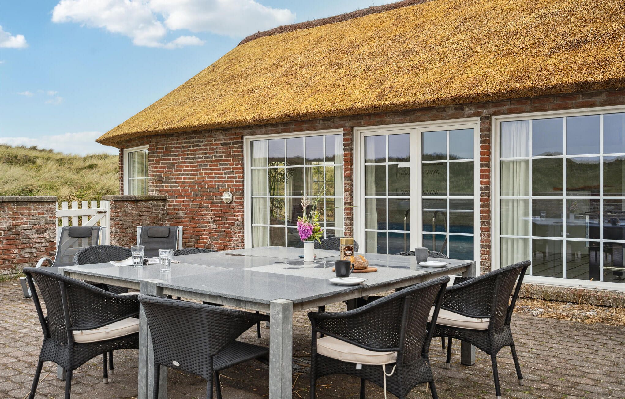 A patio with a table and chairs, a thatched roof, and large windows.