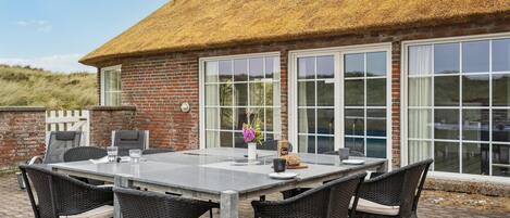 A patio with a table and chairs, a thatched roof, and large windows.