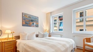 A bedroom with a bed, bedside table, lamp, and a painting on the wall. - Villa Aquamarina Whg. 13, BALCONY w. LAKE VIEW, CHAIR - Villa Aquamarina, 1st floor (Heringsdorf)