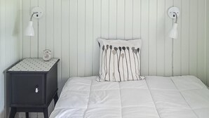 Un letto rifatto con un piumone bianco, un cuscino a righe e un comodino con una sveglia e una lampada.