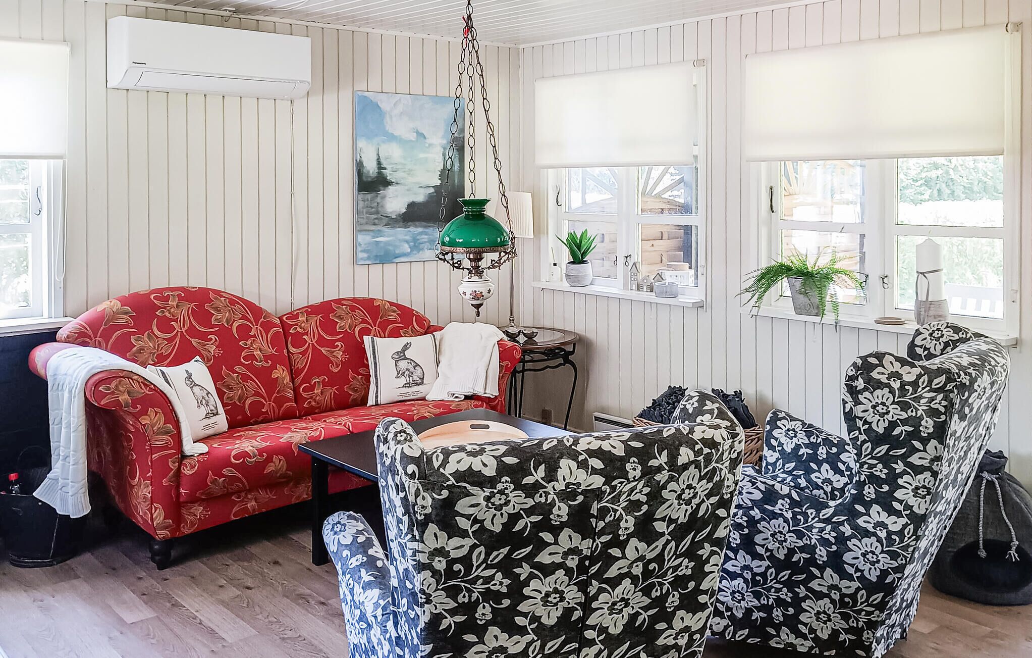 Un salón acogedor con un sofá rojo, sillones estampados, una mesita y una lámpara colgante.