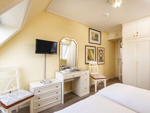 Ein Schlafzimmer mit Schreibtisch, Stuhl, Bett, Kleiderschrank und Bildern an der Wand.