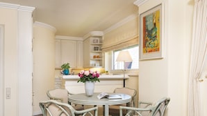 A dining area with a round table, four wicker chairs, a vase with flowers, and a window with a lamp. - Nautilus 12 from A&M - Nautilus 12 (Kampen (Sylt))