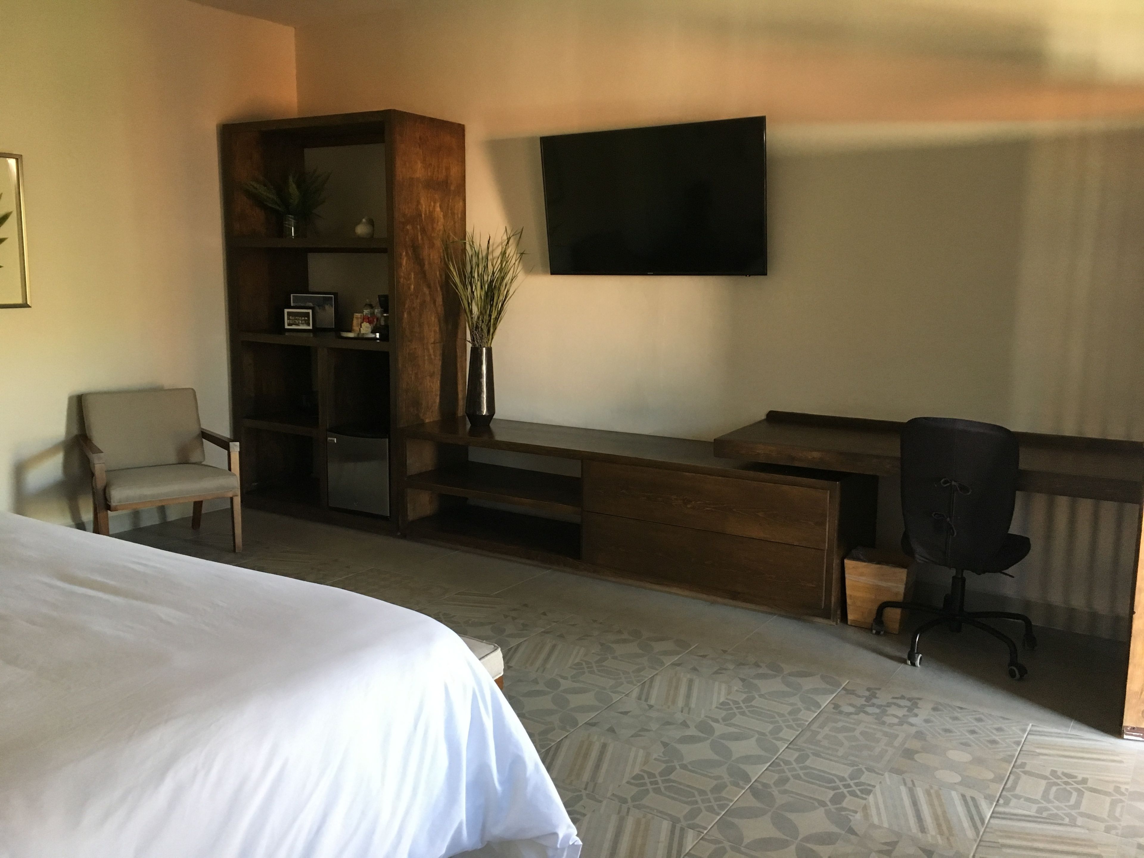 Una camera d'albergo con un letto, una scrivania con sedia, una televisione e una libreria.