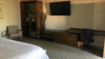 Una camera d'albergo con un letto, una scrivania con sedia, una televisione e una libreria.