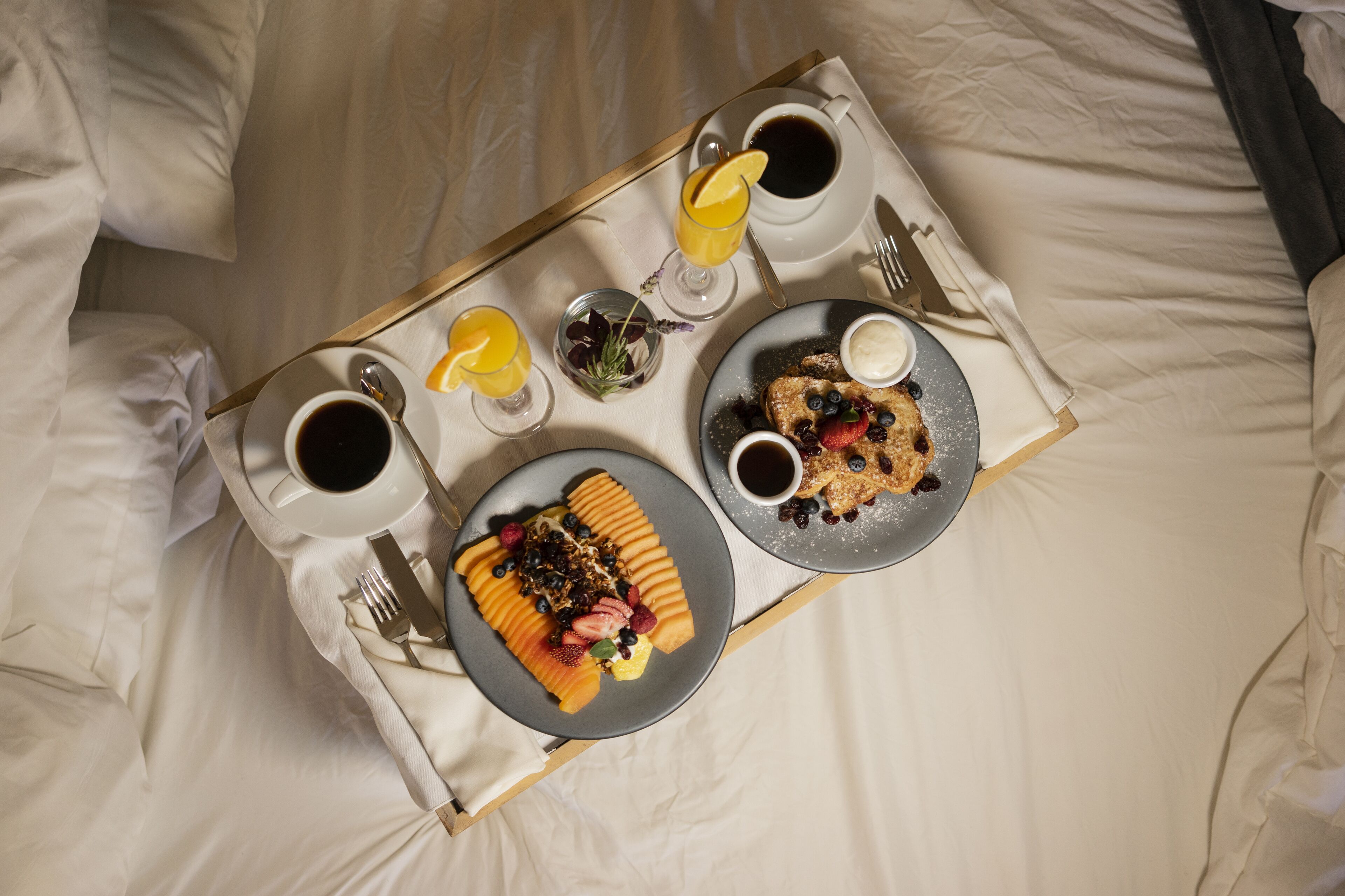 Bandeja de desayuno con panqueques, fruta y café sobre la cama.