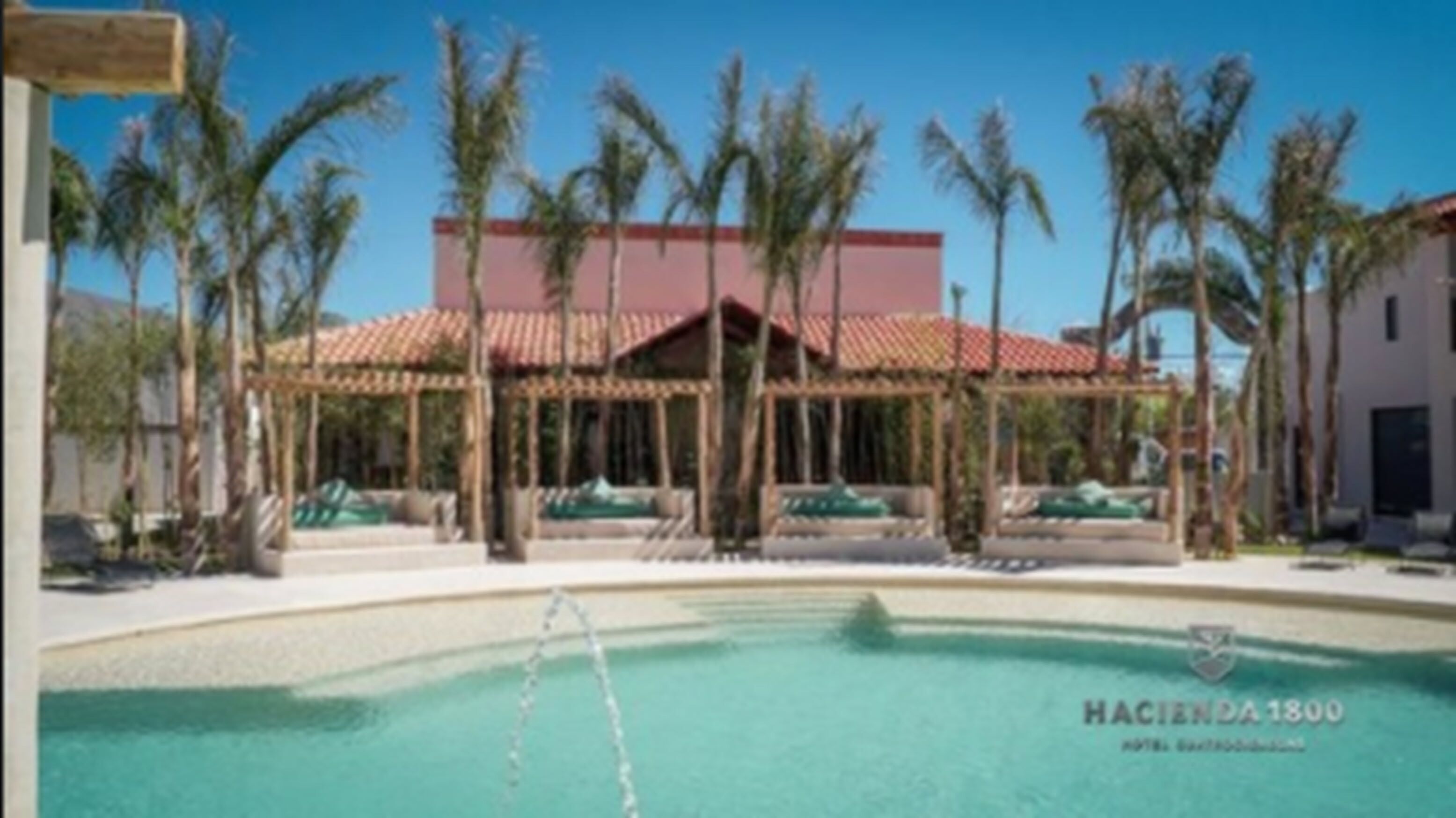 A hotel with a swimming pool, palm trees, and a red-roofed building.