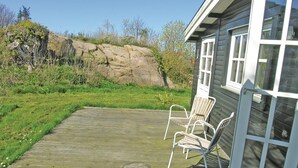 Een houten terras met twee stoelen, een rotsformatie en een huis met ramen.
