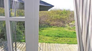 Uitzicht vanuit een raam, met een houten terras en een gazon met struiken.