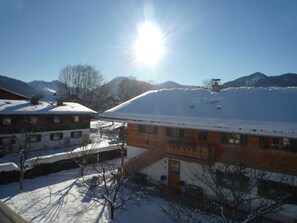 A building with a snow-covered roof, a staircase leading to the entrance, and mountains in the background. - Apartment, 1st floor, No. 2, south and large west-facing balcony - Gästehaus Johanna (Bad Wiessee)