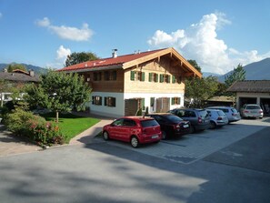 A two-story building with a red-tiled roof, parked cars, and a clear sky. - Apartment, 1st floor, No. 2, south and large west-facing balcony - Gästehaus Johanna (Bad Wiessee)