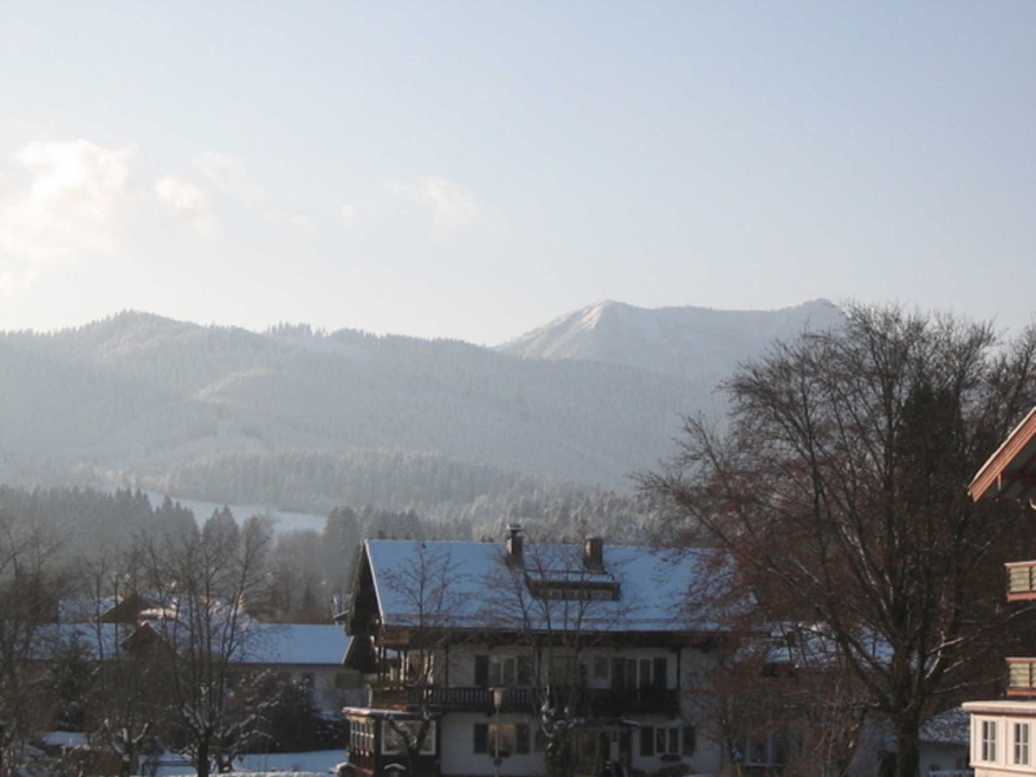A traditional chalet-style building with a snow-covered roof, situated in a mountainous area with a lake in the background.