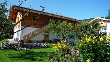 Ein Holzhaus mit rotem Ziegeldach, einer Treppe und einem Garten mit gelben Blumen.