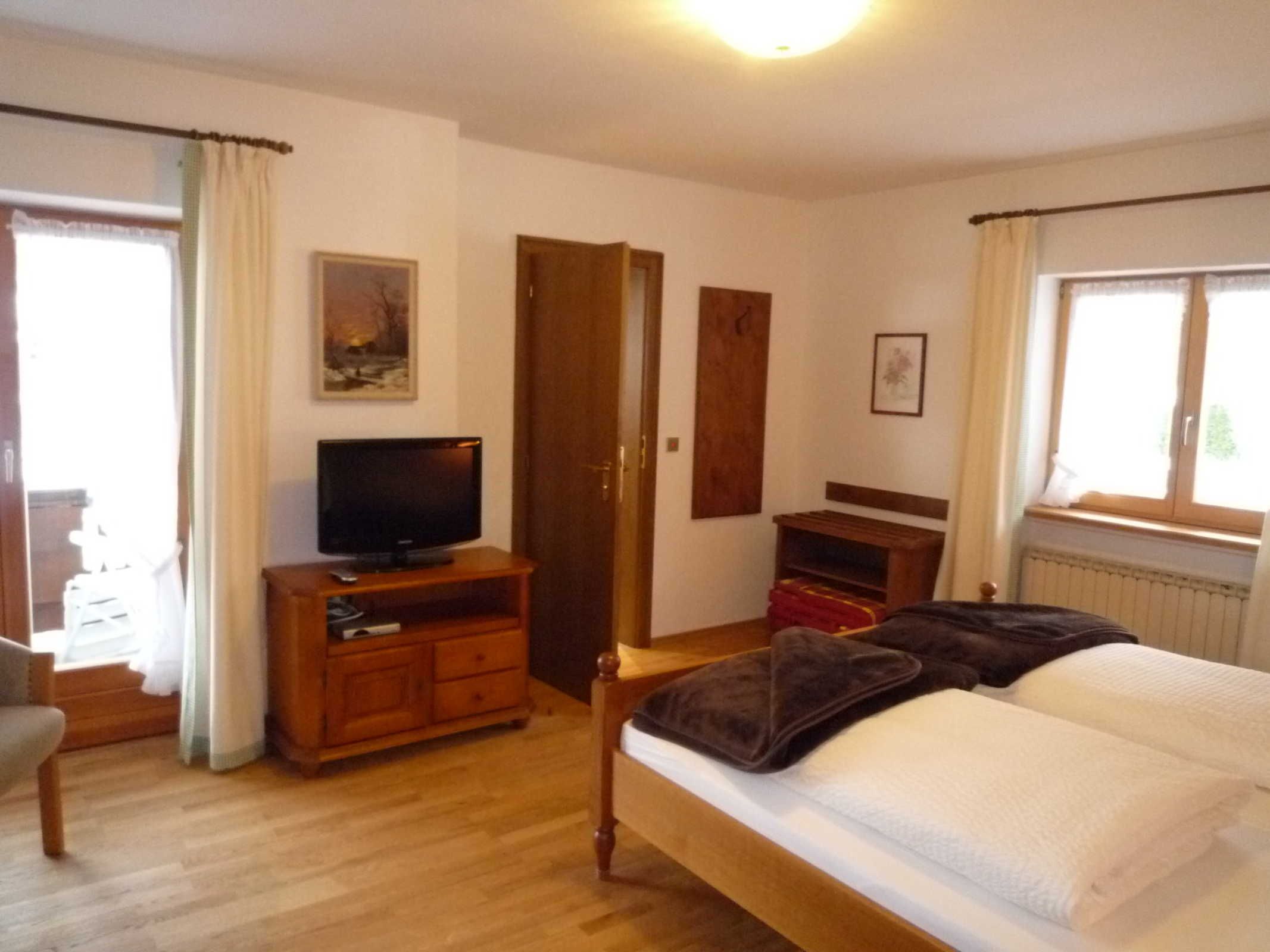 Ein Schlafzimmer mit einem Bett, einem Fernseher auf einem Holzboden, einer Tür und einem Fenster.