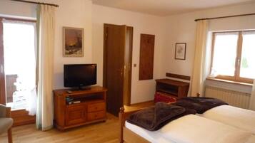 Ein Schlafzimmer mit einem Bett, einem Fernseher auf einem Holzboden, einer Tür und einem Fenster.