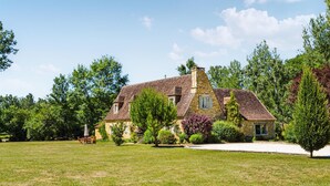 A stone house with a sloped roof, surrounded by a grassy lawn and trees. - Cozy home in La Cassagne (La Cassagne)