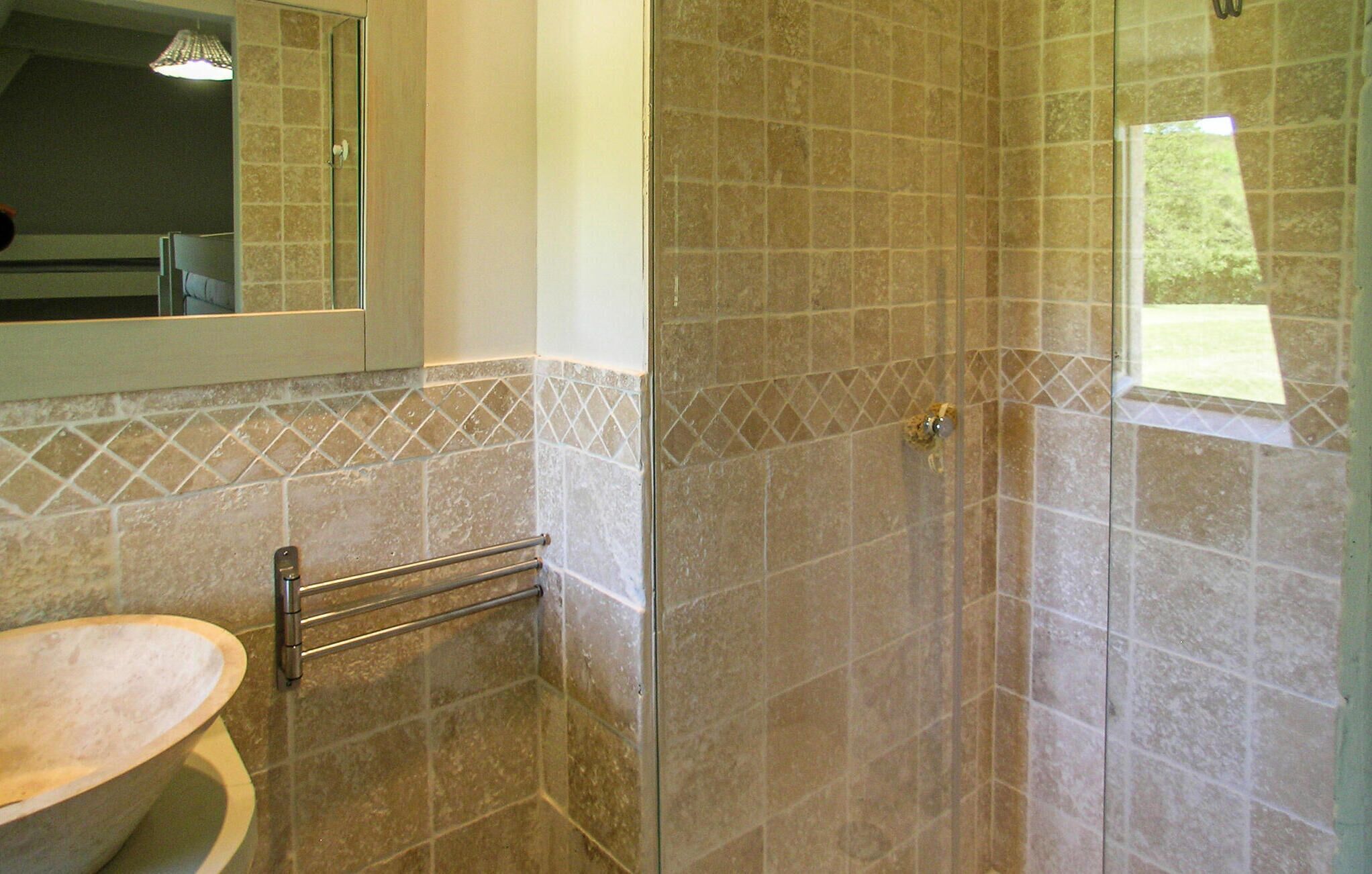 Casa de banho com sanita, cabine de duche em vidro e parede revestida a mosaico com padrão de losangos.