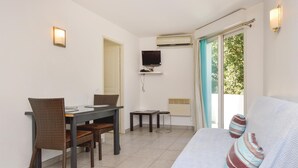 Une pièce comprenant un coin repas, un téléviseur fixé au mur, une fenêtre avec des rideaux et un canapé agrémenté d’un coussin à rayures.