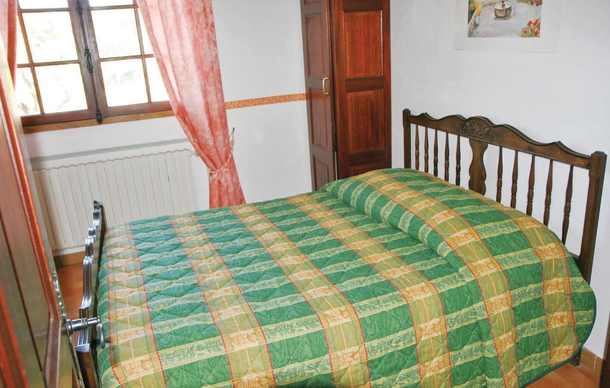 A bedroom with a wooden bed frame, a green and yellow checkered bedspread, a window with a curtain, and a radiator.