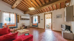 A spacious living room with a red sofa, a coffee table, and a TV. There is a wooden ceiling and a door leading to an outdoor area.
