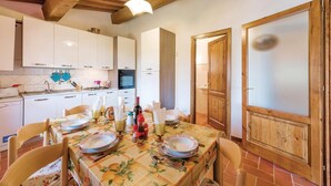 A dining area with a table set for four, a kitchen in the background, and a wooden door with frosted glass panels.