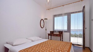 Ein Schlafzimmer mit Bett, Schreibtisch, Stuhl, Lampe und einem Fenster mit Blick.