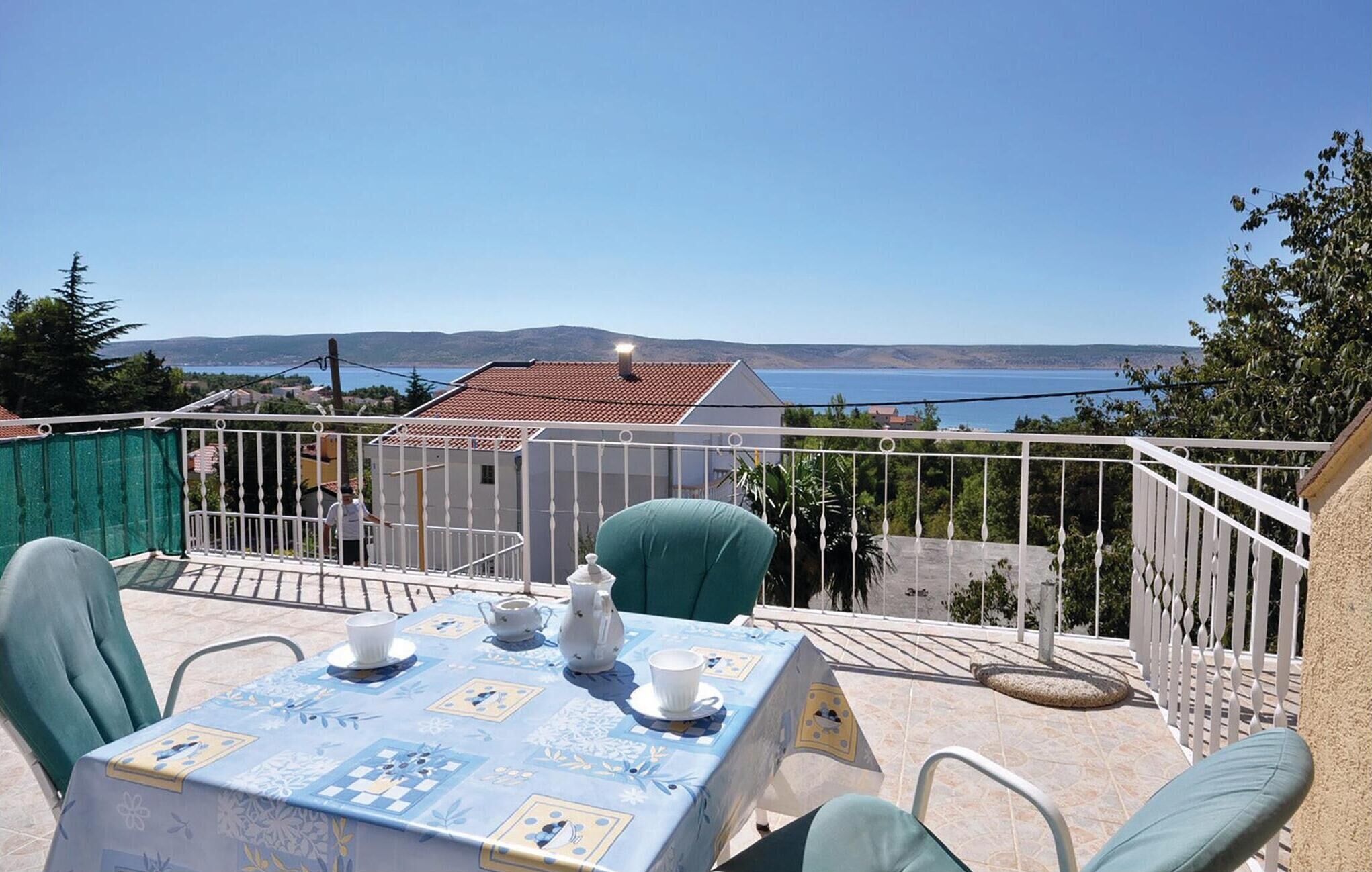 A balcony with a table set for two, overlooking a scenic view of the sea and hills.