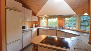 A modern kitchen with a central island, wooden cabinets, and large windows offering views of greenery. - Beautiful home in Væggerløse with sauna (Væggerløse)
