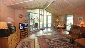 A cozy living room with a television, wooden furniture, and large windows offering a view of the outdoors. - Beautiful home in Væggerløse with sauna (Væggerløse)