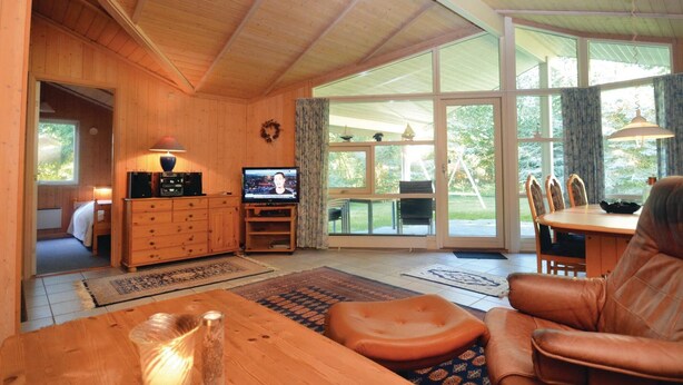 A cozy wooden interior with a television, wooden furniture, and large windows offering a view of the outdoors. - Beautiful home in Væggerløse with sauna (Væggerløse)