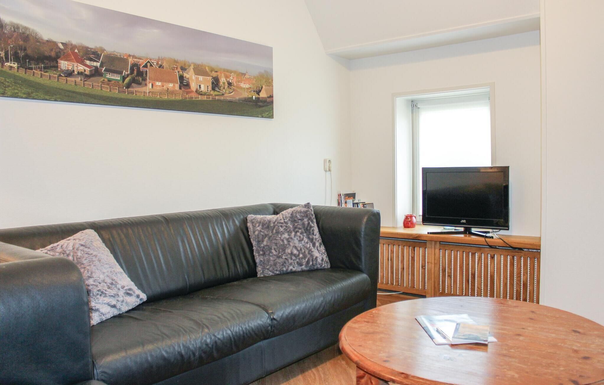 A living room with a leather sofa, a round wooden coffee table, a flat-screen TV, and a painting of a village on the wall.