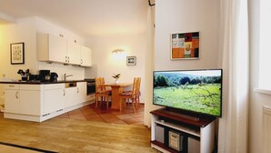 Una cocina moderna con armarios blancos, una mesa de comedor con sillas y un televisor de pantalla plana sobre un mueble.