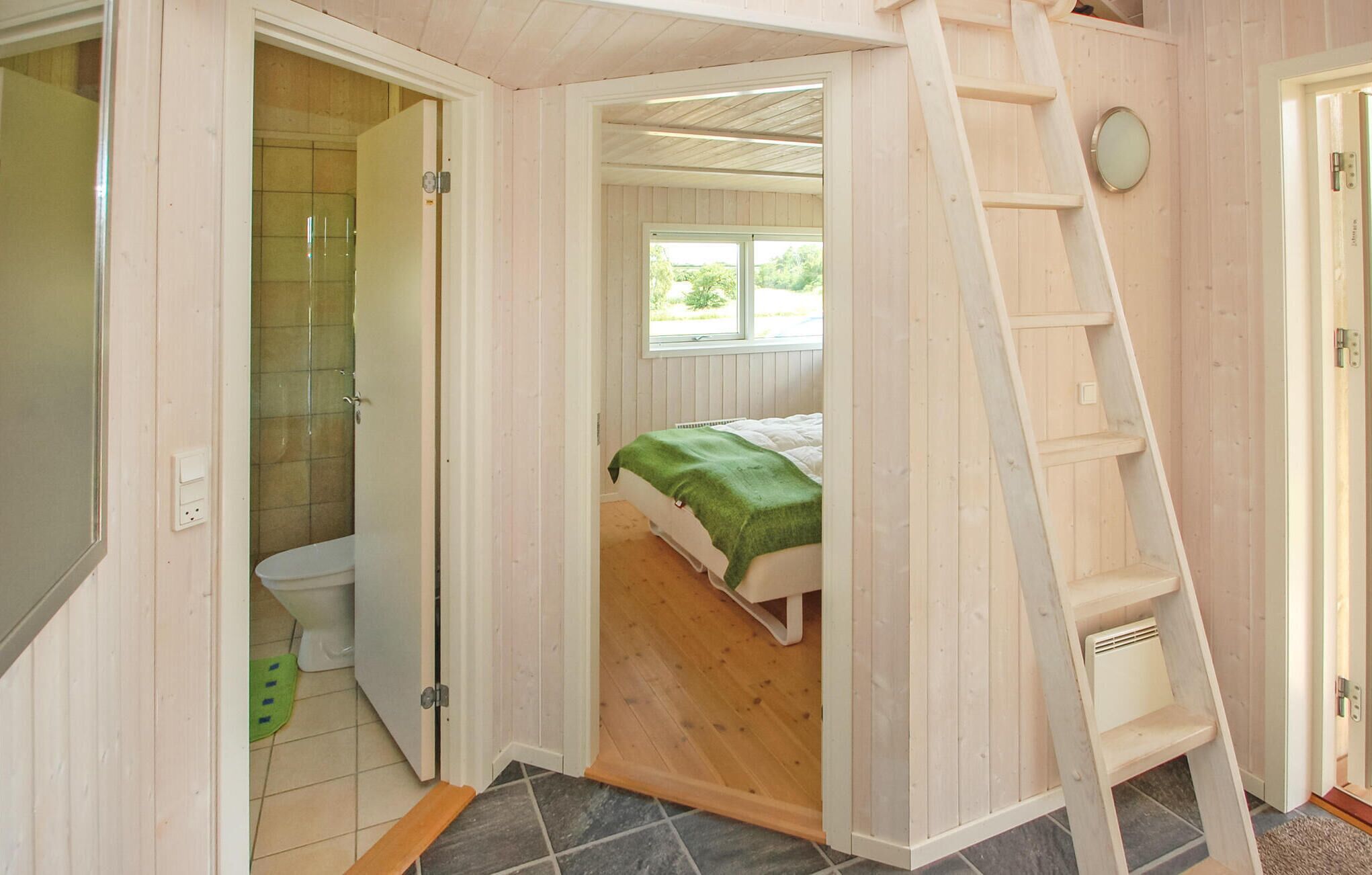 A bedroom with a bed, a window, a ladder, and a bathroom with a toilet and shower.