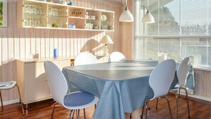 Uma sala de jantar com parede de madeira, prateleiras de vidro e uma janela grande com persianas.