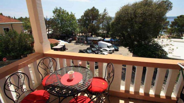 Ein Balkon mit Tisch und Stühlen, mit Blick auf einen Parkplatz und Bäume.