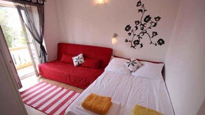 Ein Zimmer mit einem roten Sofa, einem weißen Bett mit zwei Kissen, einem Streifen Teppich und einer Wanddekoration.