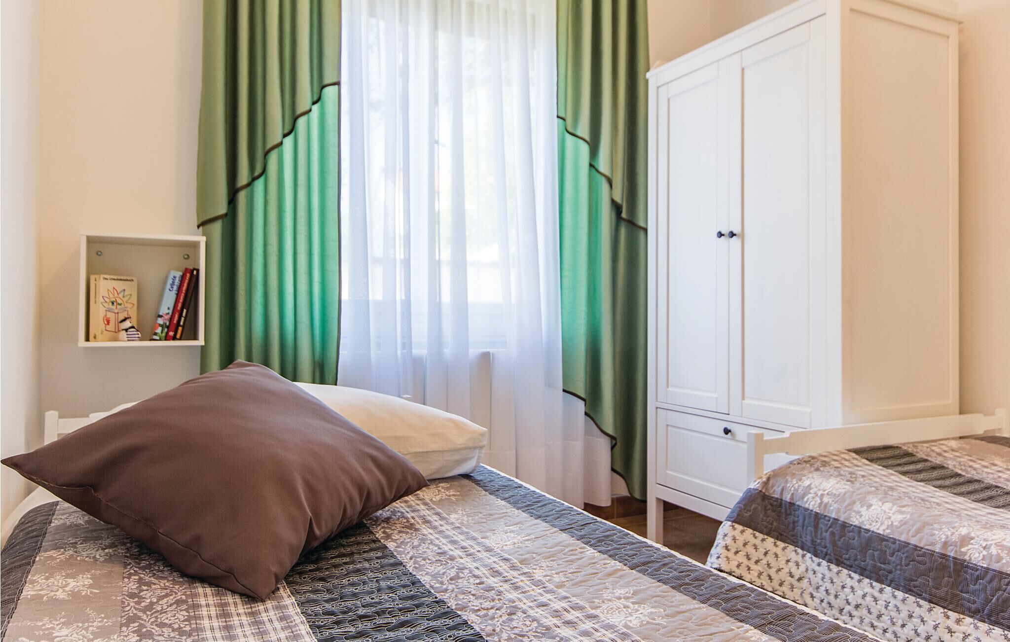 A bedroom with two beds, a wardrobe, a bookshelf, and green curtains.