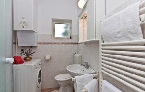 Ein kleines Badezimmer mit Waschmaschine, Toilette, Waschbecken und Handtuchhalter.